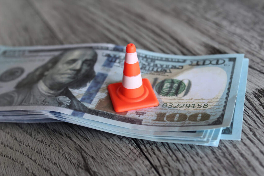 $100 bills with a small orange traffic cone, symbolizing legal or financial caution.