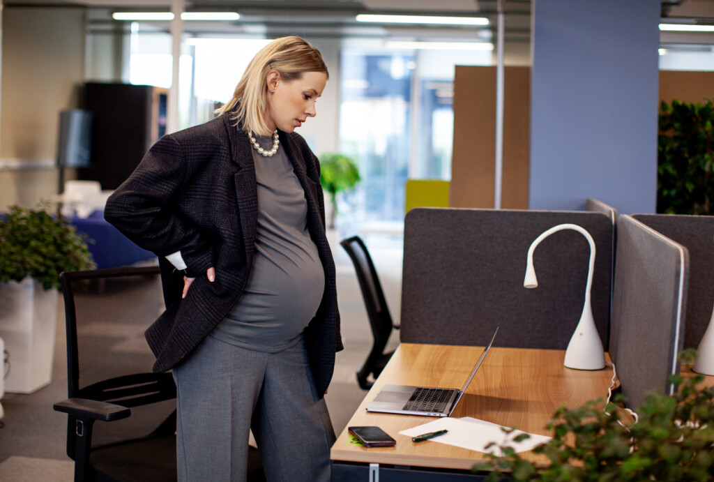 Pregnant office worker standing in cubicle